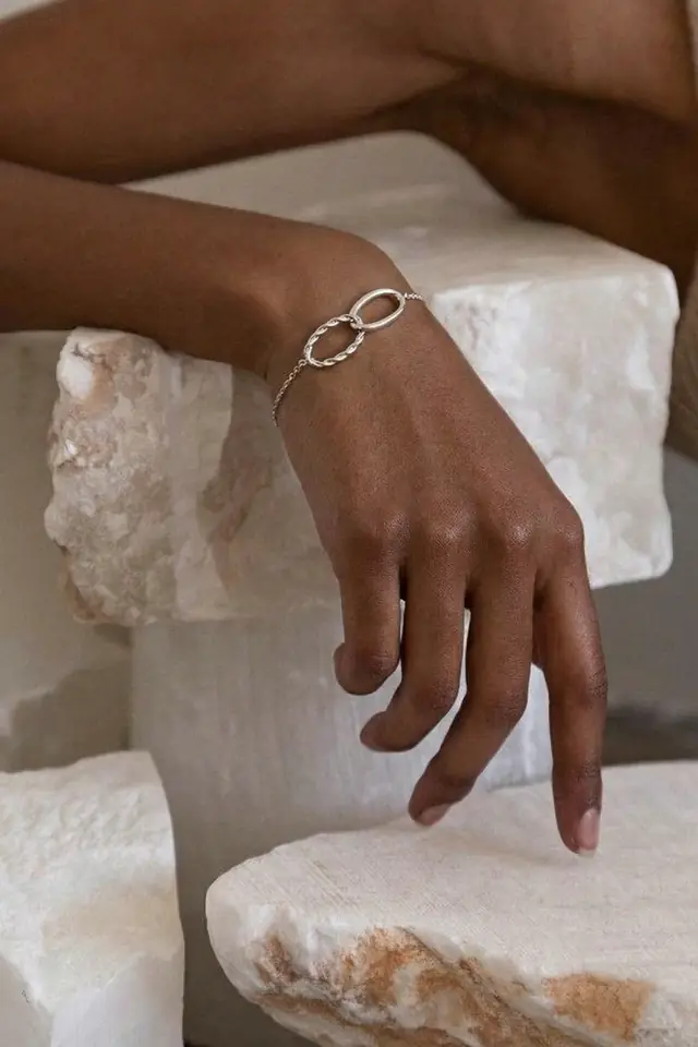 A hand wearing a silver bracelet, resting on white marble.