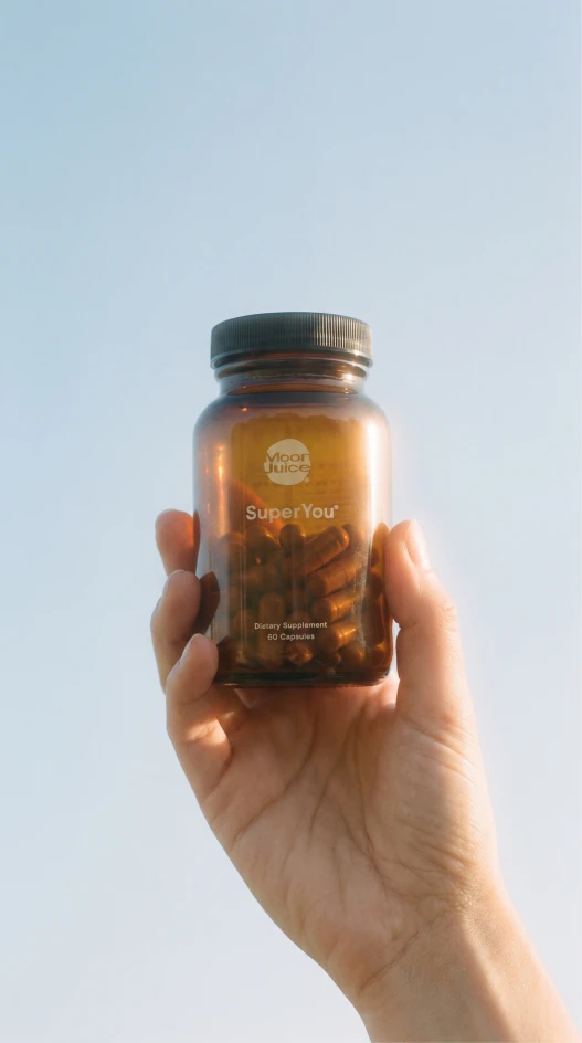 Hand holding an amber wellness bottle against a pale blue sky.