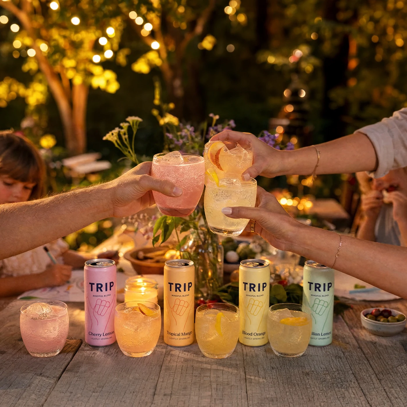 Friends raising glasses around a table with pastel TRIP cans